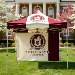 Fraternity event tent with full-width custom vinyl backdrop banner displayed on a university lawn in spring.